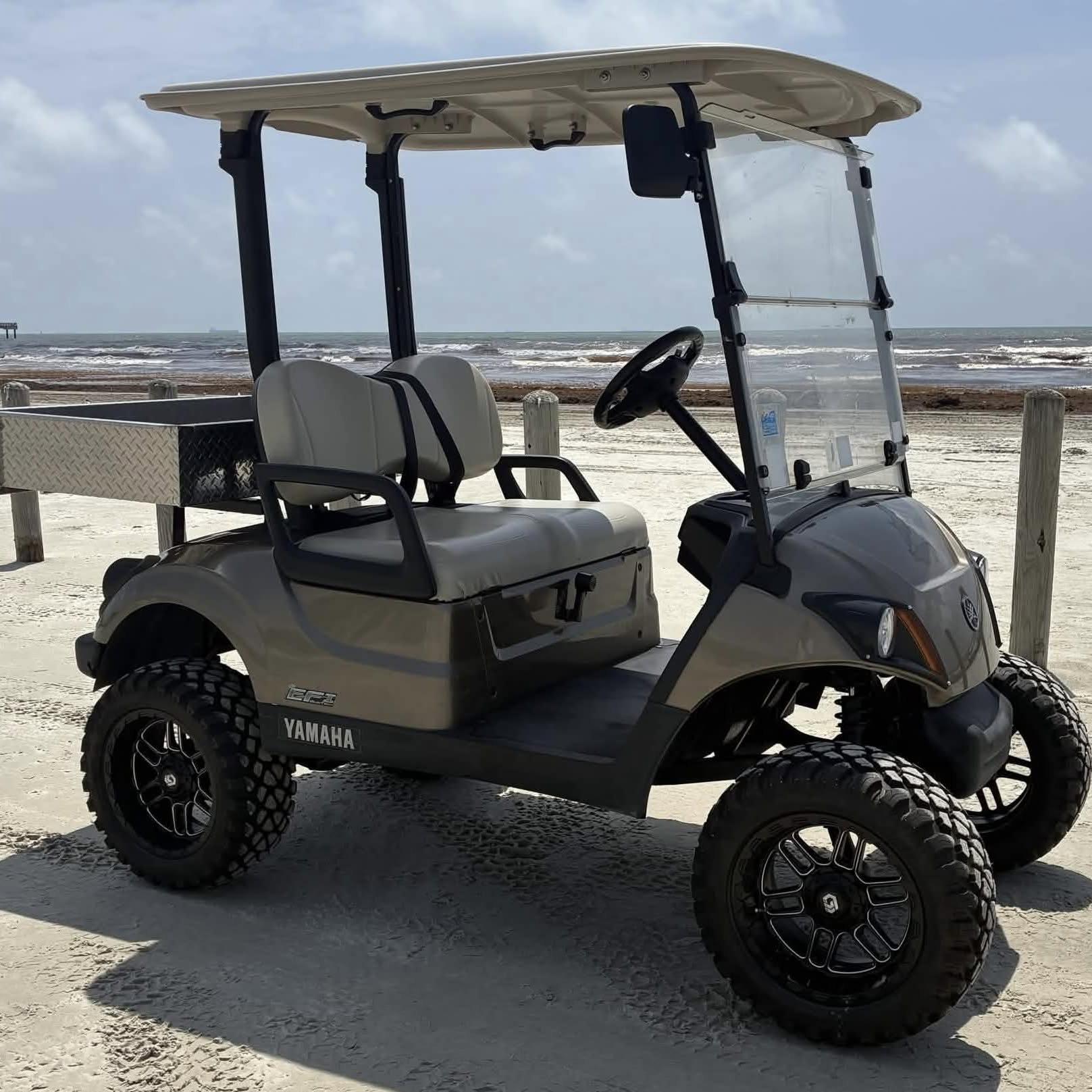 Bronze Yamaha 2-passenger cart with a diamond-plate cargo bed on the Port Aransas beach